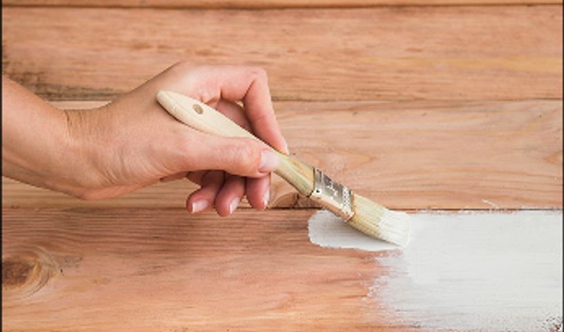 A hand using a brush to paint wood with white paint