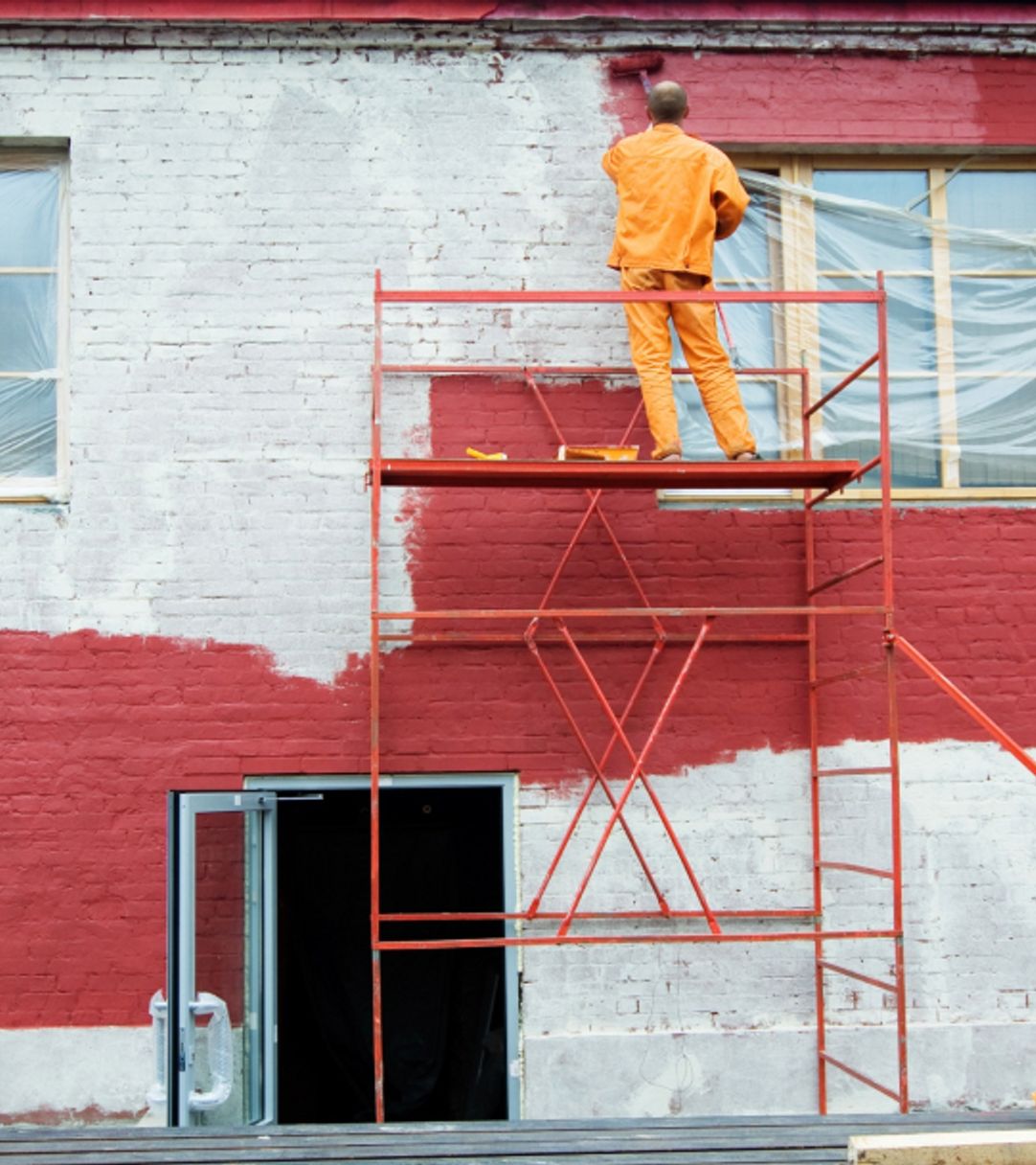 Worker painting the outside of a building red